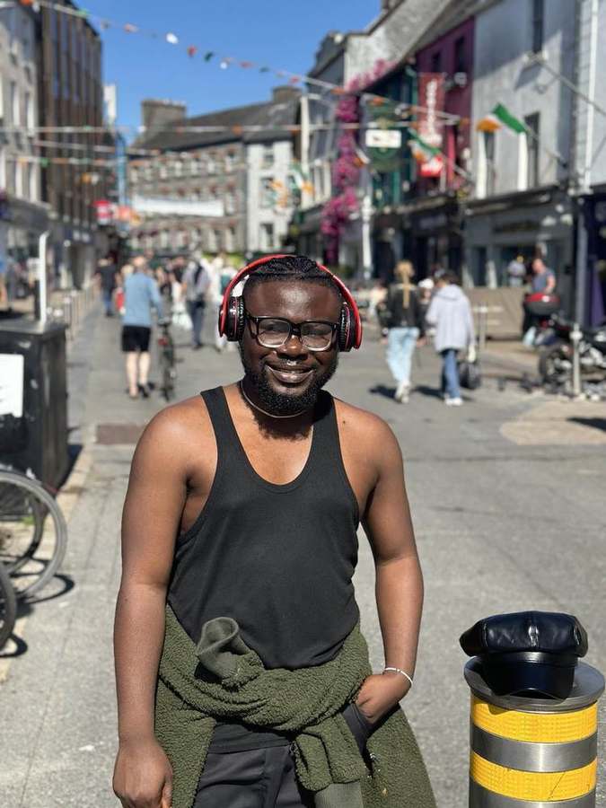 Elvis Kwame Ofori standing on a sunny street in Galway wearing headphones